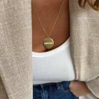 The Amour Necklace from AB Paris features a round golden pendant inscribed with "Amour," symbolizing love and affection.