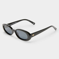 Slimline '90s-inspired oval sunglasses in shiny black with dark gray lenses, featuring a modern flat profile and gold metal hardware.