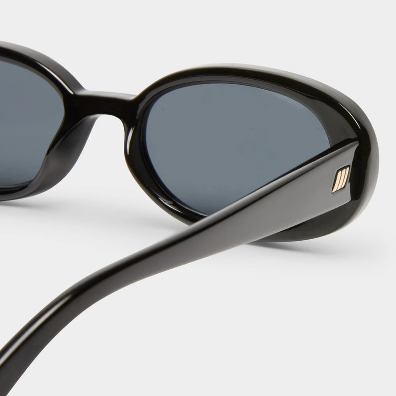 Slimline '90s-inspired oval sunglasses in shiny black with dark gray lenses, featuring a modern flat profile and gold metal hardware.