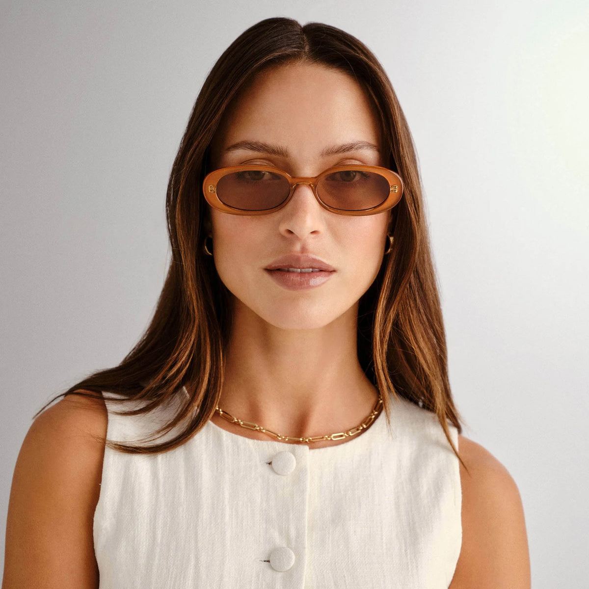 Slim, oval sunglasses with a '90s-inspired design, featuring a modern flat profile and Le Specs gold metal hardware. Petite fit, ideal for narrower face shapes. Layered caramel frame with tonal-tinted lenses. Made from lightweight, impact-resistant polycarbonate with shatterproof, scratch-resistant lenses.